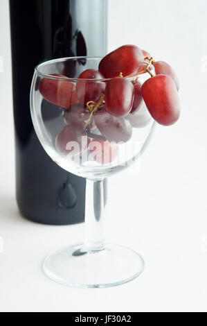 Un verre à vin rempli de raisins rouges en face d'une bouteille de vin rouge. Portrait (verticale). Banque D'Images