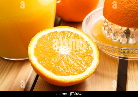 Une moitié d'orange à l'avant-plan avec presse-agrumes, d'orange et de l'ensemble pot à jus derrière sur une table de planches de bois. Banque D'Images