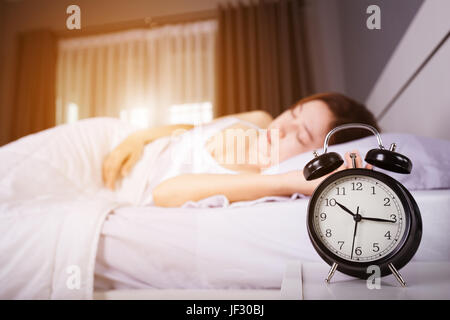 Afficher l'horloge 10h00. Et la femme dort sur le lit avec la lumière du soleil du matin Banque D'Images