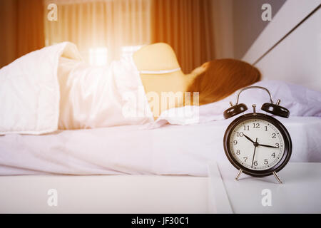 Afficher l'horloge 10h00. Et la femme dort sur le lit avec la lumière du soleil du matin Banque D'Images