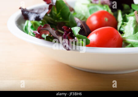 Un bol blanc salade de laitue rouge, y compris les tomates, roquette et, sur une table en bois clair. L'orientation horizontale (paysage). Banque D'Images