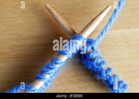 Gros plan (macro) de fil bleu pâle de suture sur une paire d'aiguilles à tricoter en bois, posé sur l'autre sur une table en bois. Banque D'Images