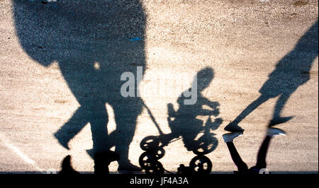 Silhouettes floues et les ombres d'une famille avec deux enfants à pied, un sur un petit vélo trois roues, à l'envers Banque D'Images