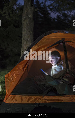 L'homme regardant son smartphone dans une tente. Banque D'Images