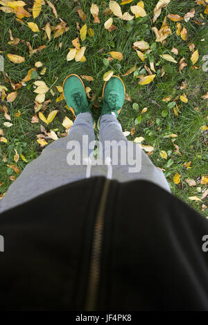 Pieds sur un pré vert avec les feuilles d'automne Banque D'Images