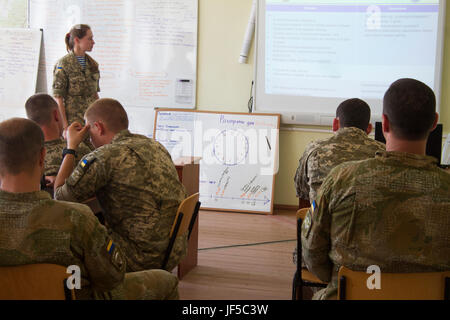 Un officier ukrainien présente sa partie de l'analyse de mission bref au cours de la formation en classe à l'viv centre d'instruction au combat le 30 mai 2017, alors que le personnel de la CCT de l'Ukraine et les mentors affecté à la formation Group-Ukraine multinationales conjointes d'évaluer sa performance. Américains, Britanniques, Polonais, Lituaniens, et des mentors canadiens mènent à la formation du personnel en classe dans le cadre de l'JMTG-U La mission globale de professionnalisation et la construction de la capacité de formation de l'armée ukrainienne. Banque D'Images