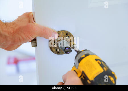 Carpenter à l'installation de verrouillage avec la perceuse électrique à l'intérieur de porte en bois Banque D'Images