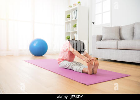 Peu de jeunes asiatiques fille assise sur le plancher en bois avec mat redresser ses jambes et pieds mains prendre corps avec le yoga stretch fit sport à la Banque D'Images