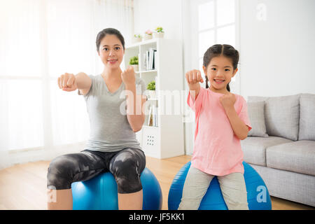Sportives avec des enfants de parents dans le salon assis sur le ballon et montrant le poing contre poing et avant de faire l'action pour améliorer le mode de vie à l'heure h Banque D'Images