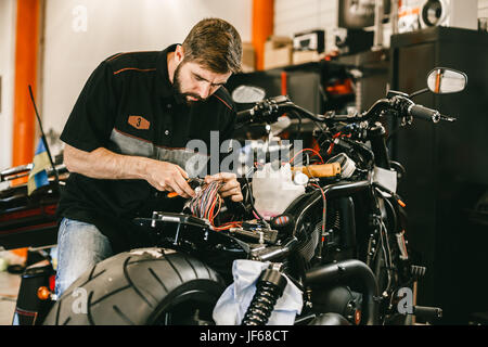 Mécanicien moto professionnel travaille avec l'électronique, coupe les fils. Beau travail de mécanicien dans un atelier de réparation de vélo. Banque D'Images