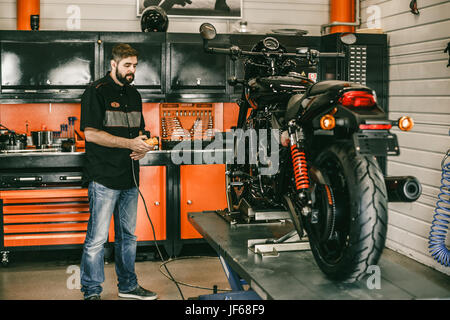 Mécanicien moto professionnelle soulève une moto sur l'ascenseur. L'homme en appuyant sur Haut et Bas pour passer en atelier de réparation de vélo. Banque D'Images