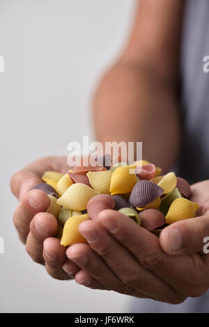 Jeune homme avec une pile de conchiglie crus italiens, pâtes, coquillages de différentes couleurs : jaune, rouge comme d'habitude faite avec de la tomate et vert fait avec Banque D'Images