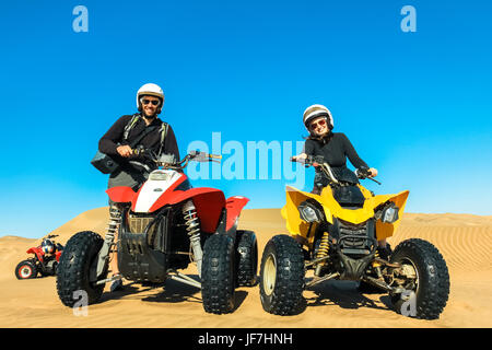 Quad conduisant des personnes - happy smiling couple bikers en désert de sable. Banque D'Images