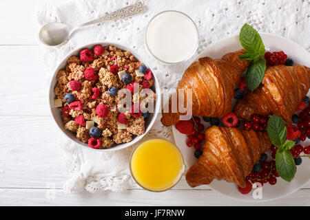 Muesli avec des baies et des croissants, du lait et du jus d'orange sur la table horizontale vue du dessus. Banque D'Images