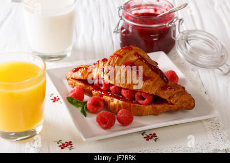 Croissant avec les framboises et confiture, jus et lait close-up sur la table horizontale. Banque D'Images