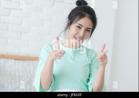 Jeune femme asiatique attrayant vert usure chiffon occasionnel gesturing action positive tout en étant assis dans la chambre. lazy girl activité sur dimanche matin. Banque D'Images