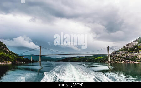 Le pont qui relie la rive du fjord en Norvège sur le fond de ciel dramatique et les vagues du navire. Banque D'Images