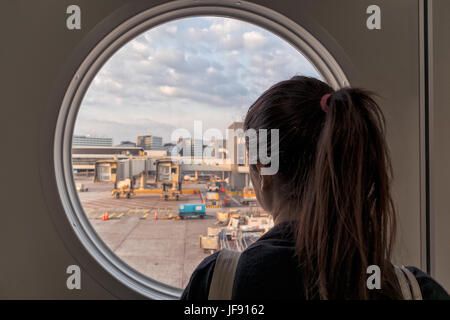 Fille de regarder à travers un fenêtre ronde à l'aéroport de Schiphol à Amsterdam. Banque D'Images