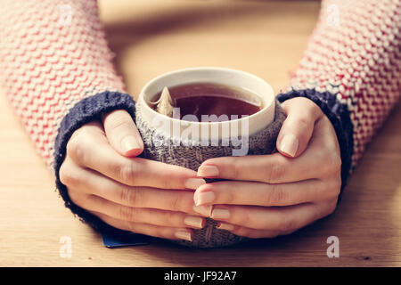 Tasse de thé chaud réchauffement de la Woman's hands en rétro cavalier de laine. Table en bois Banque D'Images