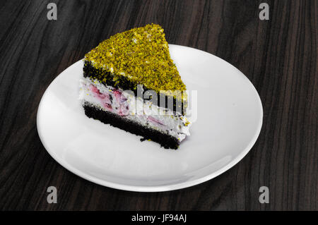 Berry et gâteau au chocolat surmontée à la pistache servi dans une assiette blanche sur une table en bois Banque D'Images