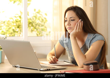 L'apprentissage des élèves sérieux en ligne regarder du contenu dans un ordinateur portable assis dans une table dans sa chambre à la maison Banque D'Images