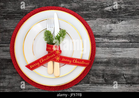 Table de dîner de Noël avec des assiettes, des couverts, du ruban et le sapin sur un tapis rouge sur fond en bois vieilli. Banque D'Images