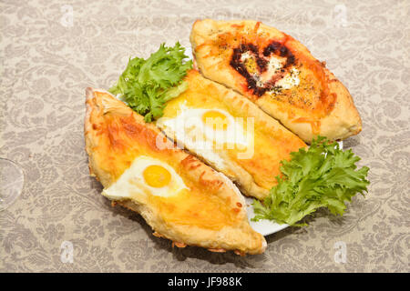 Adjara khachapuri. Plat de cuisine caucasienne sur une plaque près de feuilles de salade verte. Banque D'Images