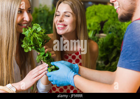 Cute blonde deux jeunes femmes dans un marché de légumes. woman smelling un bouquet de menthe fraîche au supermarché alors que le vendeur est le tenant en place Banque D'Images