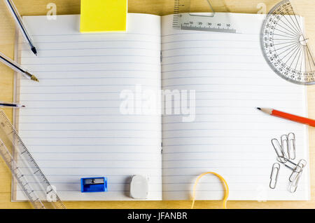 D'un coup de frais généraux de l'école a ouvert un livre d'exercices. entourée d'articles de papeterie sur un bureau en bois clair. Pages lignées fournir copie de l'espace. Banque D'Images