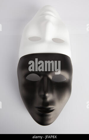 Les masques noirs et blancs réunis sur fond réfléchissant blanc. Vertical image, vue du dessus. Concept de l'anonymat.