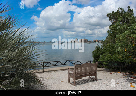 Banc en bois vide vous appelle s'asseoir et profiter de la vue sur la baie de Sarasota au pont, l'eau reflétant le ciel bleu et nuages blancs flottant. Banque D'Images
