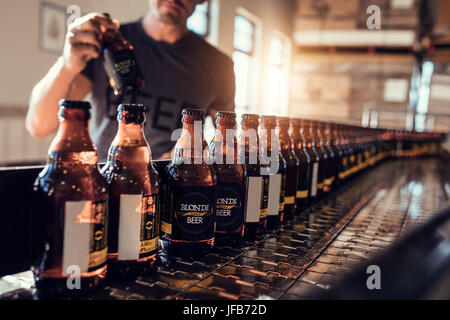 Les bouteilles de bière avec convoyeur de déménagement dans l'usine de brasserie. Jeune homme de superviser le processus de mise en bouteille de bière et de contrôle de la qualité à la fabrication pl Banque D'Images