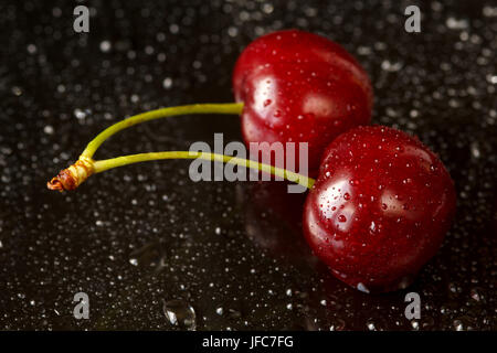 Plan Macro sur deux délicieuses cerises mûres sur un fond réfléchissant noir avec des gouttes d'eau. Profondeur de champ Banque D'Images