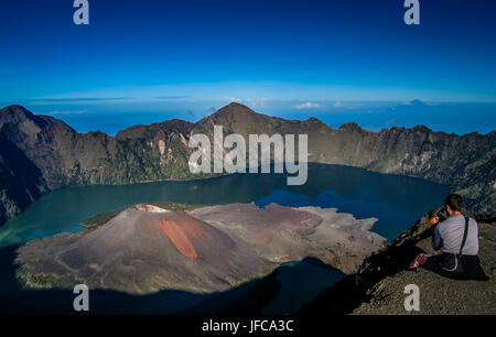 Tourist assis sur le bord du cratère du volcan Gunung Rinjani à Lombok, Indonésie Banque D'Images