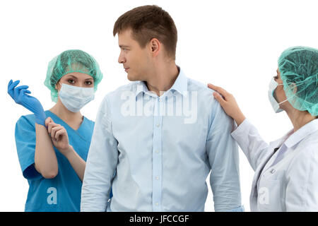 Femme médecin dans le chapeau et masque de visage de mettre sur bleu gant de protection derrière la peur du patient. Sa collègue essaie de le rassurer. Medic Banque D'Images