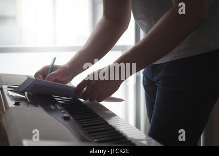 Compositeur et auteur-compositeur à écrire des notes ou des paroles sur papier au piano. Musicien écrire un morceau d'home studio sur un instrument numérique. Banque D'Images