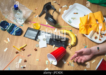 Gueule de bois après la fête. L'homme gisant sur le sol, la main visible. Corbeille, restes alimentaires, des vêtements, des talons hauts et des bouteilles partout. Accueil très malpropre. Banque D'Images