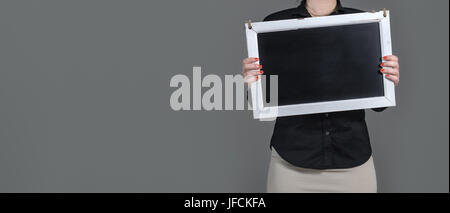 Woman holding chalkboard with copy space. Beaucoup de place pour le texte en blanc et le contenu. Fond gris foncé. Fille avec serveuse ou vêtements d'affaires Banque D'Images