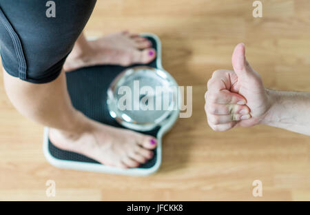 Personal trainer ou coach giving Thumbs up pour une personne debout sur l'échelle. Succès et grande réussite dans la perte de poids. L'encouragement et la motivation. Banque D'Images