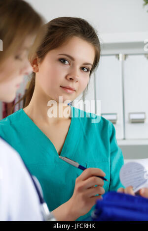 Deux belles femmes médecins médecine travaillant à leur bureau discuter de diagnostiquer et de remplissage ou d'enregistrement du patient Formulaire d'antécédents médicaux. Se médicale Banque D'Images