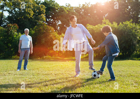 Belle vue. L'engagement enthousiaste fun playing football parent avec son fils et lui apprendre quelques trucs alors que le grand-père en regardant sa famille Banque D'Images