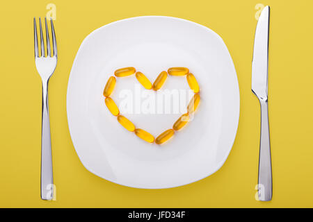 L'huile de poisson gels doux couché sur la plaque en porcelaine blanche en forme de cœur (fond jaune) Banque D'Images