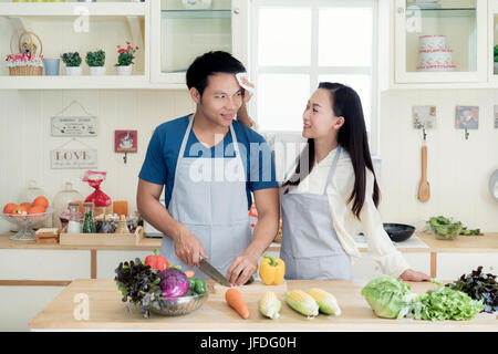 Belle jeune femme asiatique aidant à sec mari sueur sur son visage dans la cuisine à la maison. Heureux couple love concept. Banque D'Images