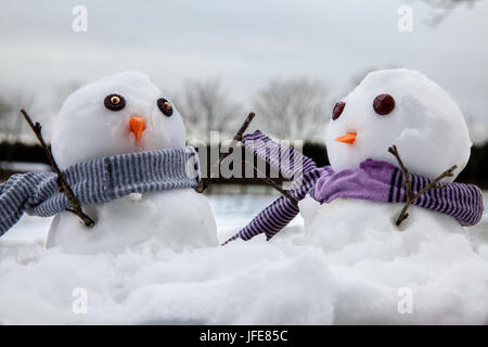 Deux bonhommes mignon portant des écharpes et leur brindille bras levés en l'air. Chutes de neige tout autour de Banque D'Images