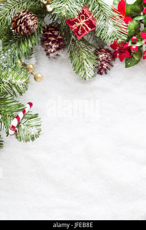 Une frontière de Noël à gauche et le haut du châssis composé de feuillage artificiel, pommes de pin et des ornments, saupoudrée de neige sur un faux s Banque D'Images