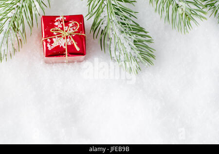 Un cadre supérieur de la frontière de Noël arbre artificiel sur les frondes de neige artificielle avec une petite boîte cadeau rouge brillant placé entre. Banque D'Images