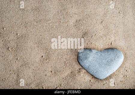 Une pierre en forme de coeur gris niché dans le sable doré en bas à droite de l'image. L'espace de copie dans le sable. Banque D'Images