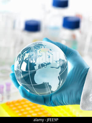 Global research, conceptual image. Scientist holding a globe avec un banc de laboratoire et la verrerie en arrière-plan. Banque D'Images