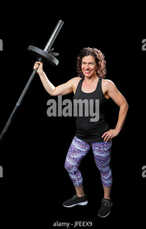 Un ajustement, l'haltérophile féminin se tient sur un fond noir, tenant une tige avec une plaque de poids. Elle pose, mais est prêt à l'épaule consécutive Banque D'Images
