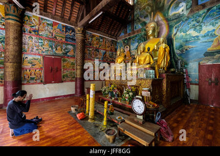 Femme en prière devant une statue de Bouddha en or à l'intérieur de la Wat Aham temple de Luang Prabang, Laos, Asie Banque D'Images